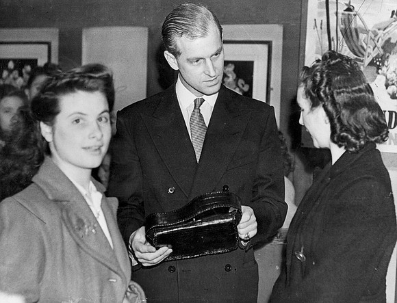 The Duke of Edinburgh examines a handbag made by girls of the leatherwork and millinery club during a visit to the Dockland Settlement. 1947.